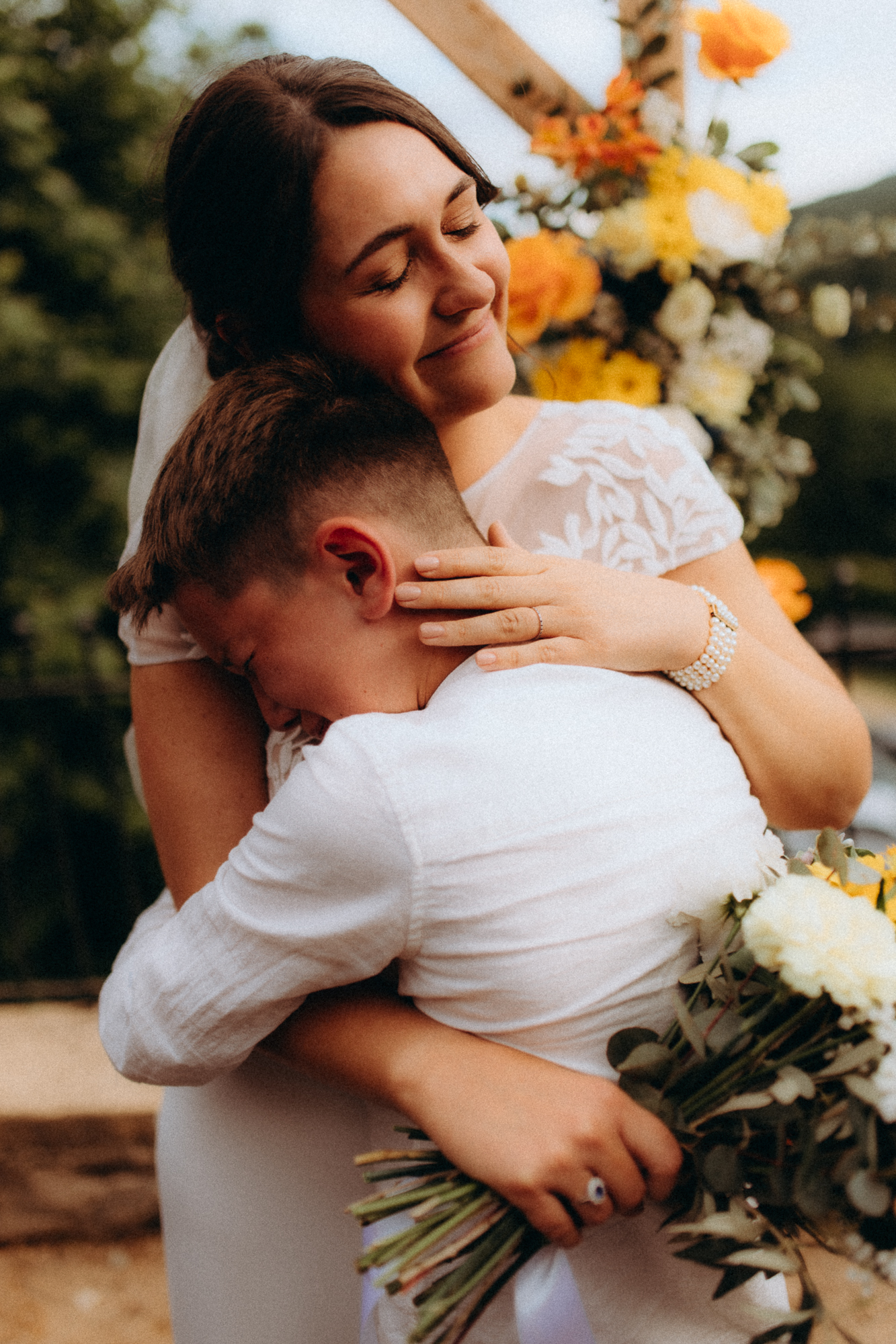 Mariée qui serre quelqu'un dans ses bras avec tendresse, bouquet de fleurs jaunes
