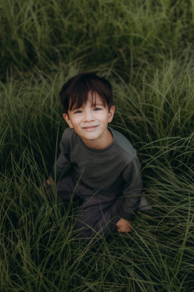 Portrait de Glenn assis dans l'herbe haute, enfant espiègle, photographe famille Chartreuse