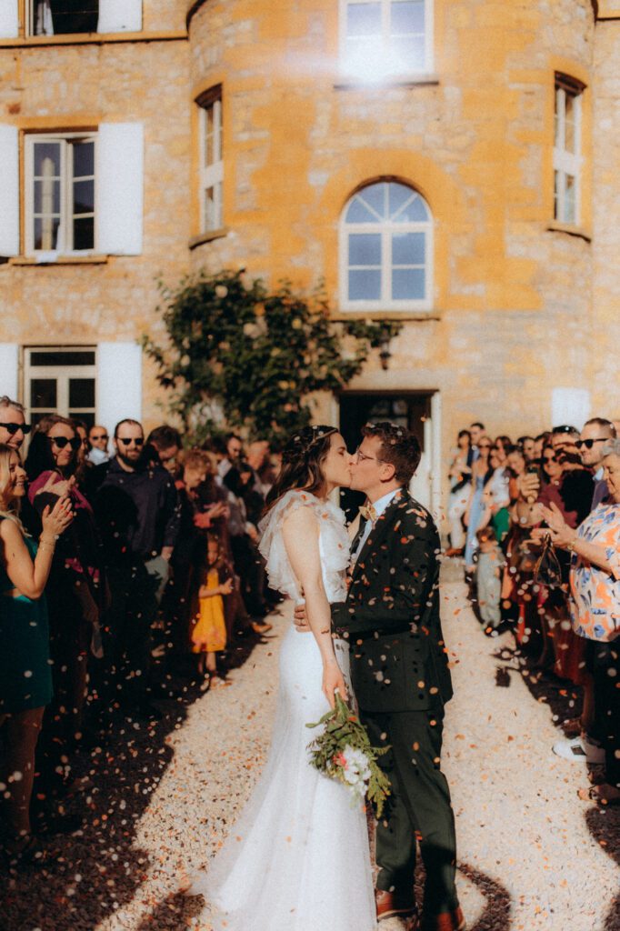 Mariés qui s'embrassent devant le domaine, entourés de leurs invités