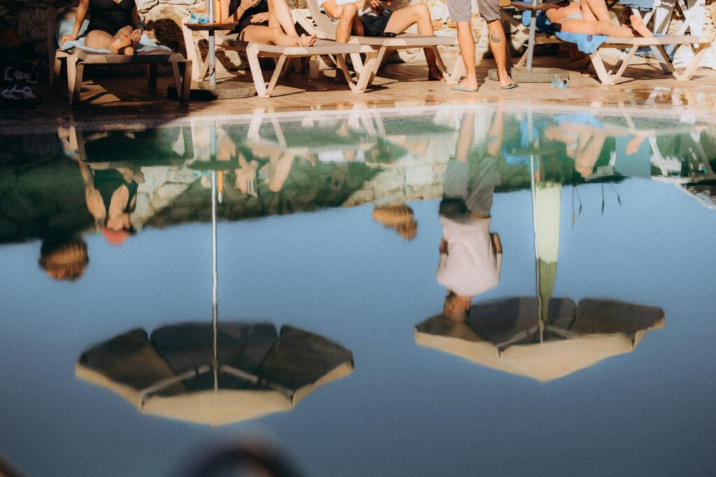 Reflet inversé de transats et de parasols dans l’eau de la piscine, invités allongés au soleil