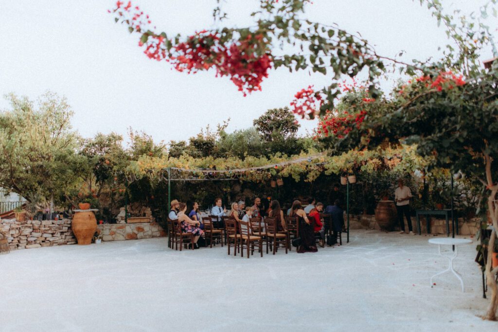 Cour de la taverne Baxès en Crète, bougainvilliers rouges et pergola de vigne, invités attablés au fond