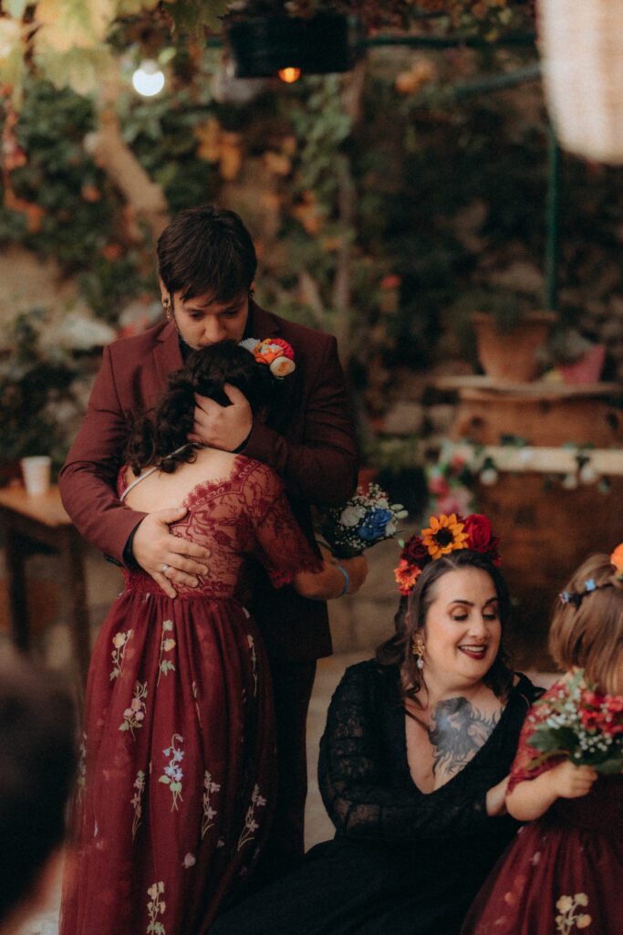 Marvin embrasse une invitée en robe rouge brodée, Elodie rit à côté