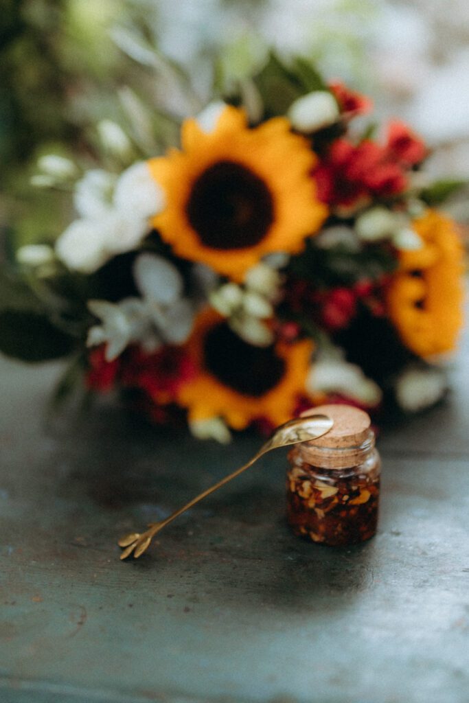 Bouquet de tournesols et de fleurs rouges à côté d’un petit pot de noix et de miel et d’une cuillère dorée