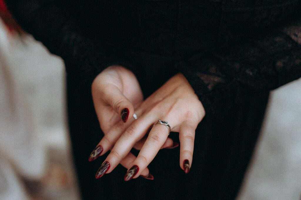 Mains de la mariée aux ongles bordeaux, alliance sur la dentelle noire de sa robe
