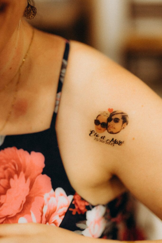 Tatouage éphémère à l’effigie des mariés avec lunettes de soleil, sur l’épaule d’une invitée